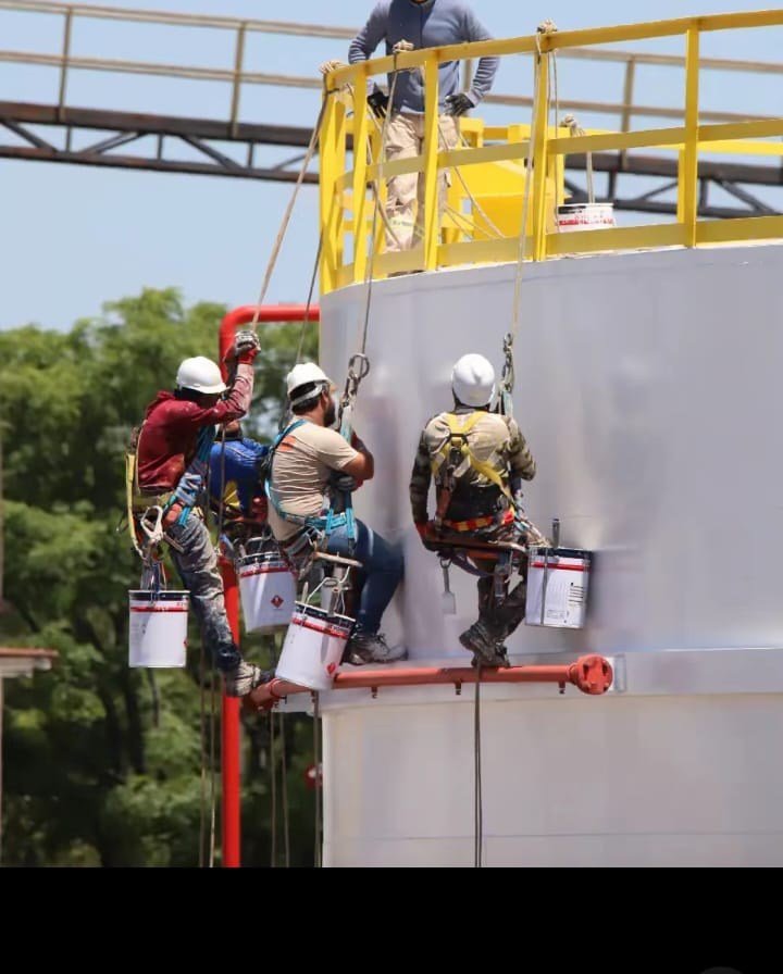 Cuadrilla de pintores suspendidos con arnés trabajando sobre un tanque